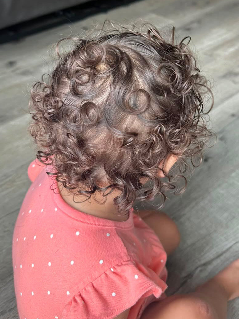 A toddler with damp curls sitting in the bath on wash day