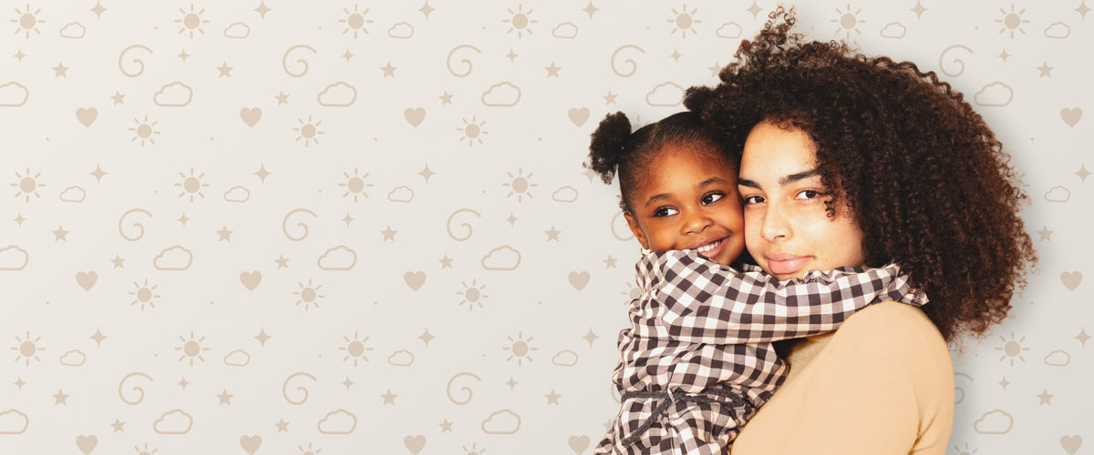 A mother holding her young daughter close, cheek to cheek, both with natural curls