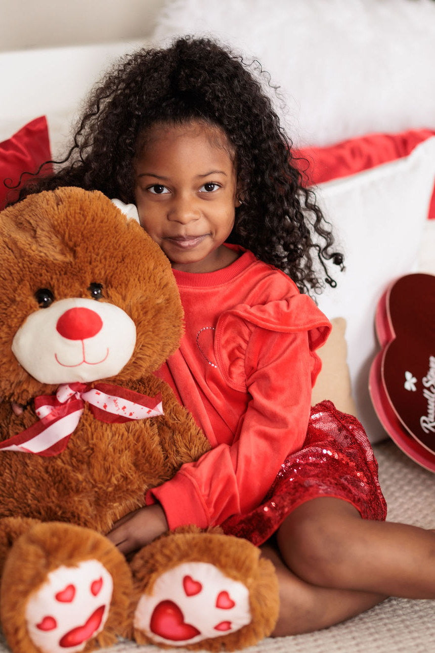 Cristina sitting on a bed holding a large teddy bear, dressed in red