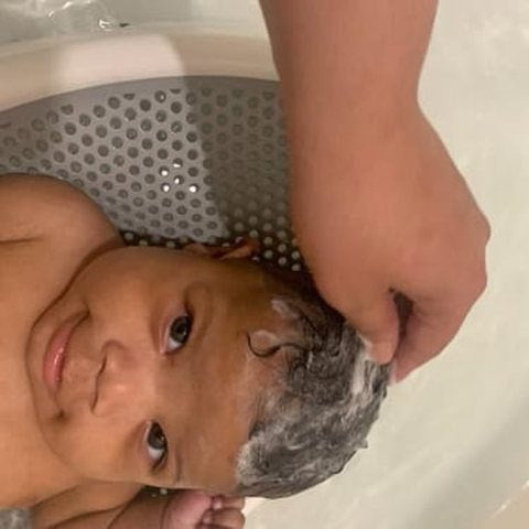 A parent washing a baby's lathered curls in the tub