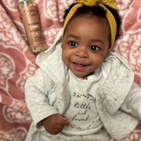 A smiling baby in a yellow headband beside the hair oil
