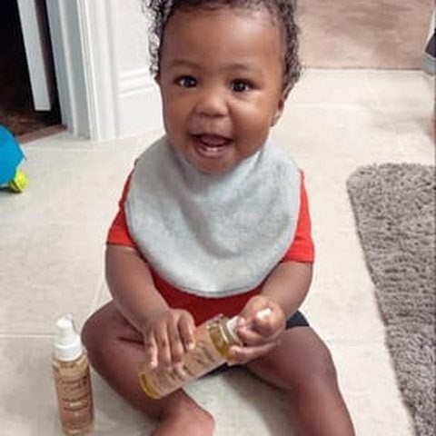 A smiling toddler holding the baby shampoo and oil
