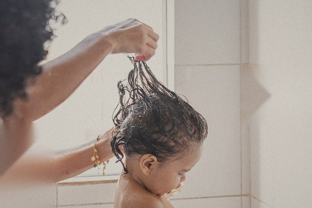 A parent lifts conditioner through a baby's wet curls so it slips through